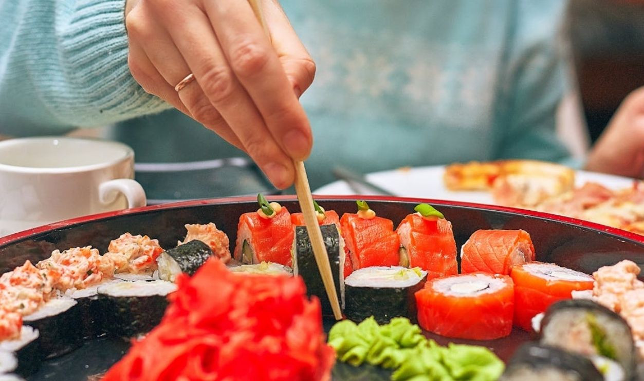 A hand skillfully picks sushi from a platter using chopsticks. Vibrant and delicious