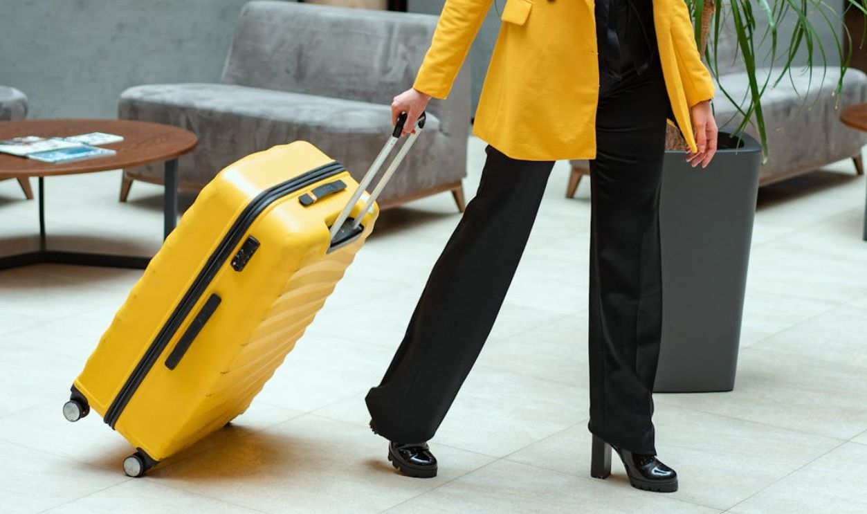 Stylish woman walking in hotel lobby pulling a bright yellow suitcase