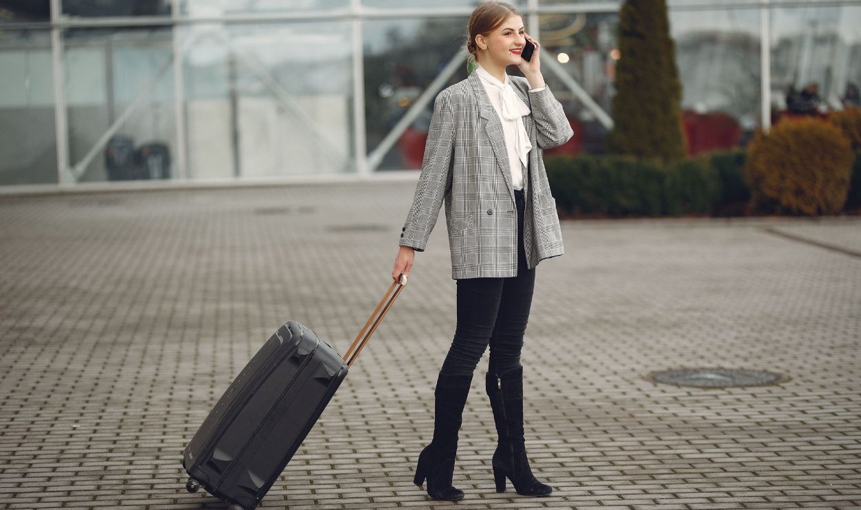 Confident businesswoman talking on phone while pulling a suitcase outdoors