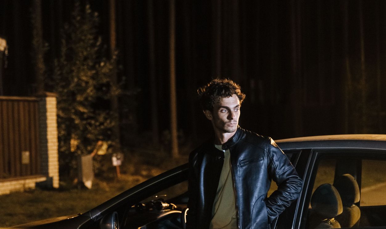 Mysterious night scene of a man beside a car, blocked by stop tape, under streetlights