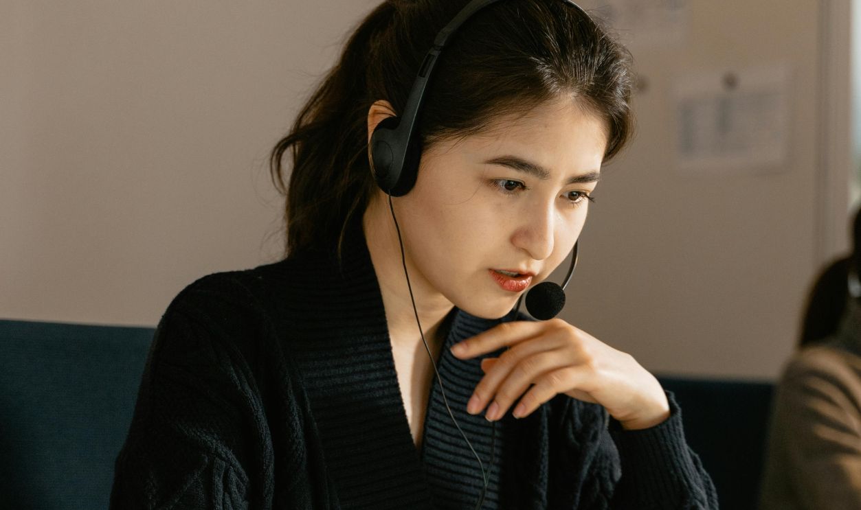 Focused female customer support agent in an office using a laptop and headset