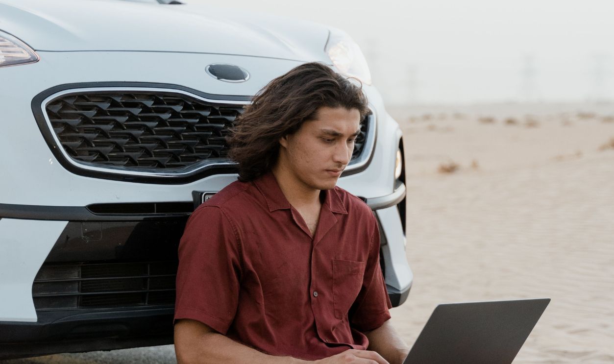 Man sitting by car on desert road with laptop, embracing remote work lifestyle