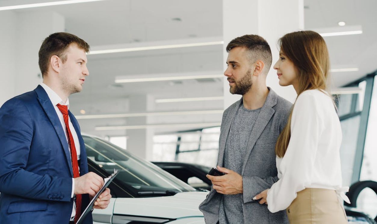 Car salesman assisting a couple in a modern showroom with a luxury car.