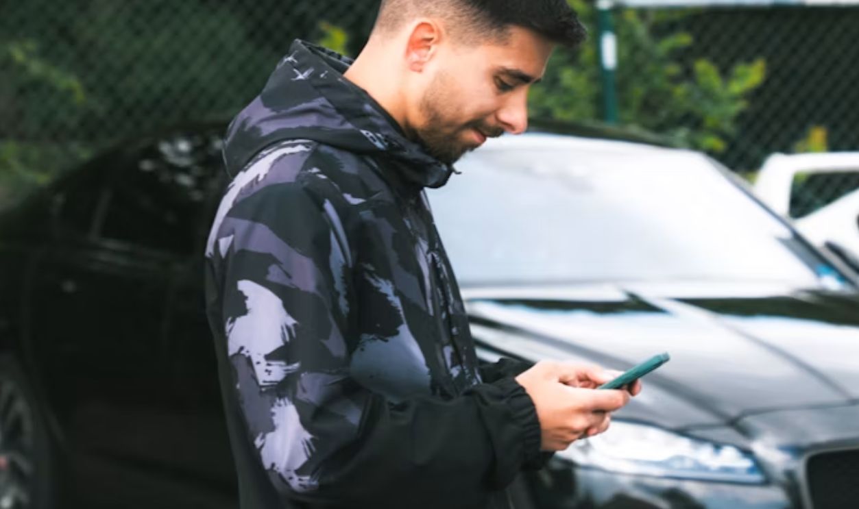 A man standing next to a car looking at his cell phone