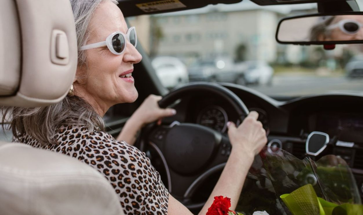 Senior woman driving a convertible, smiling and wearing sunglasses on a sunny day