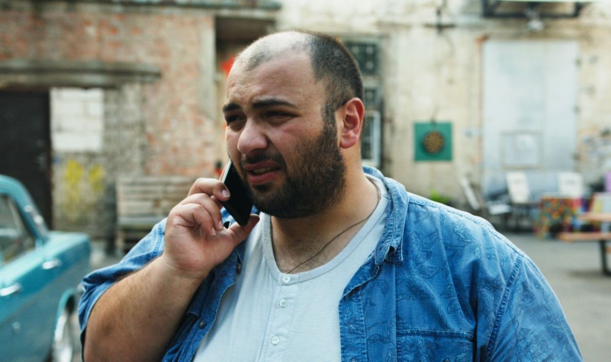 Bearded man with denim shirt using smartphone outside in urban setting
