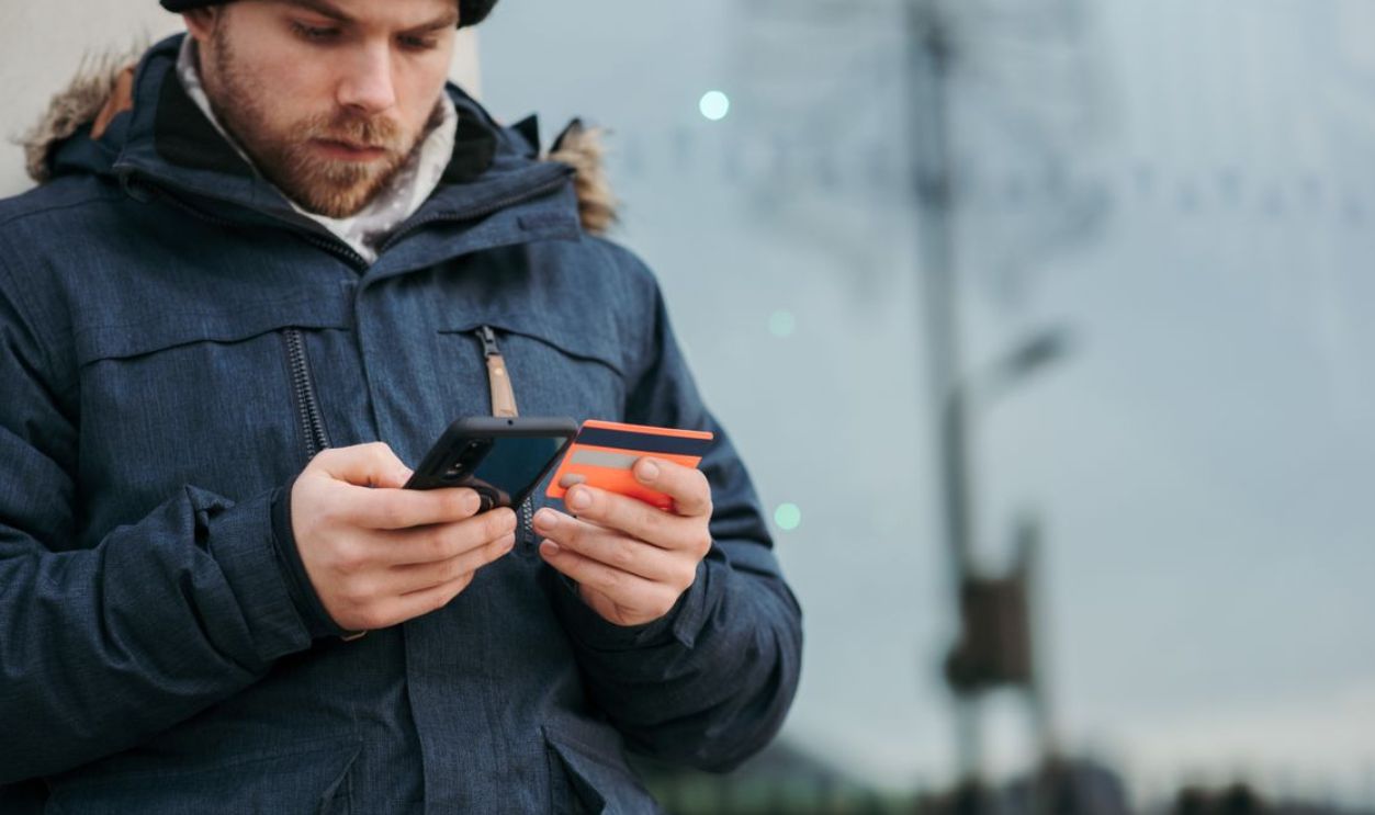 Young man using smartphone for online transaction outdoors, dressed warmly in winter attire