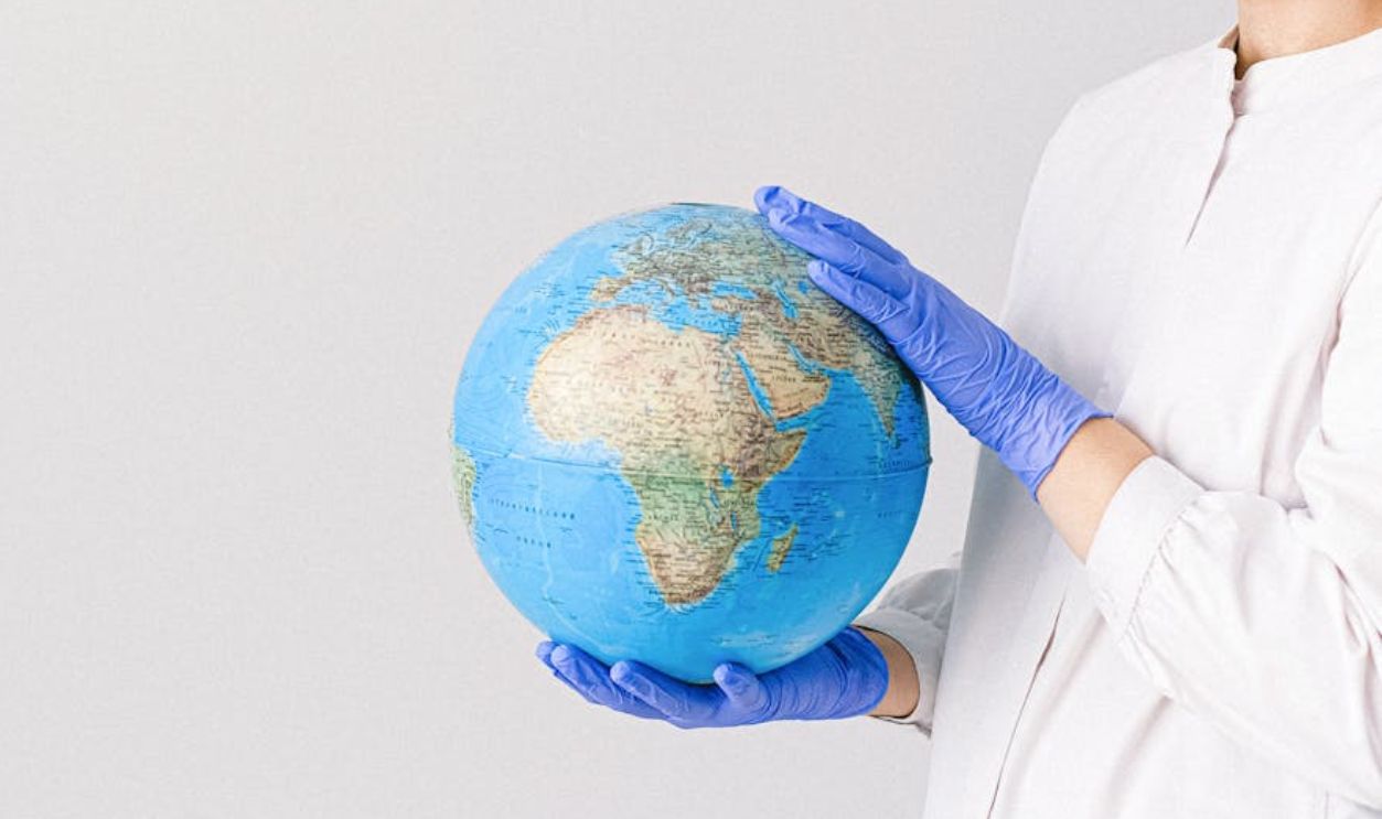 Person in mask and gloves holding a globe, symbolizing global healthcare during pandemic.