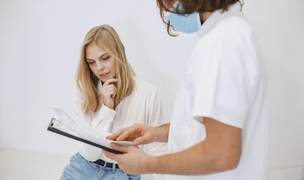 A doctor in a face mask discusses diagnosis with a patient in a clinic setting.