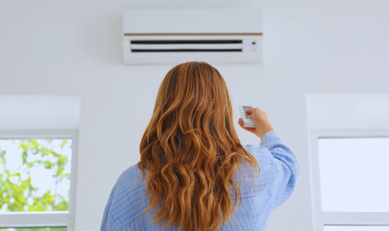 Shutterstock-2679106611, Young woman turning on air conditioner in room, back view