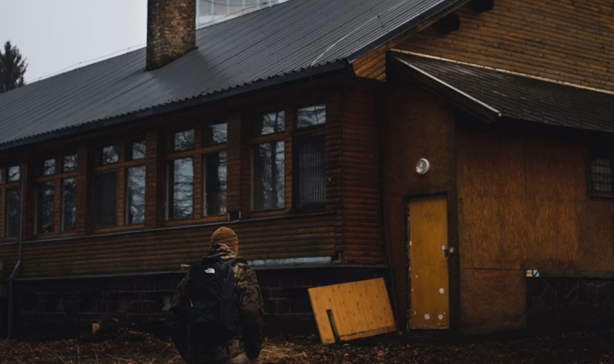 man in black jacket sitting on bench near brown wooden house during daytime