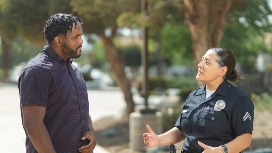 A police officer engaging warmly with a community member outdoors on a sunny day.