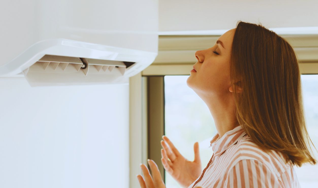 Women dying from the heat standing in front of the air conditioner.