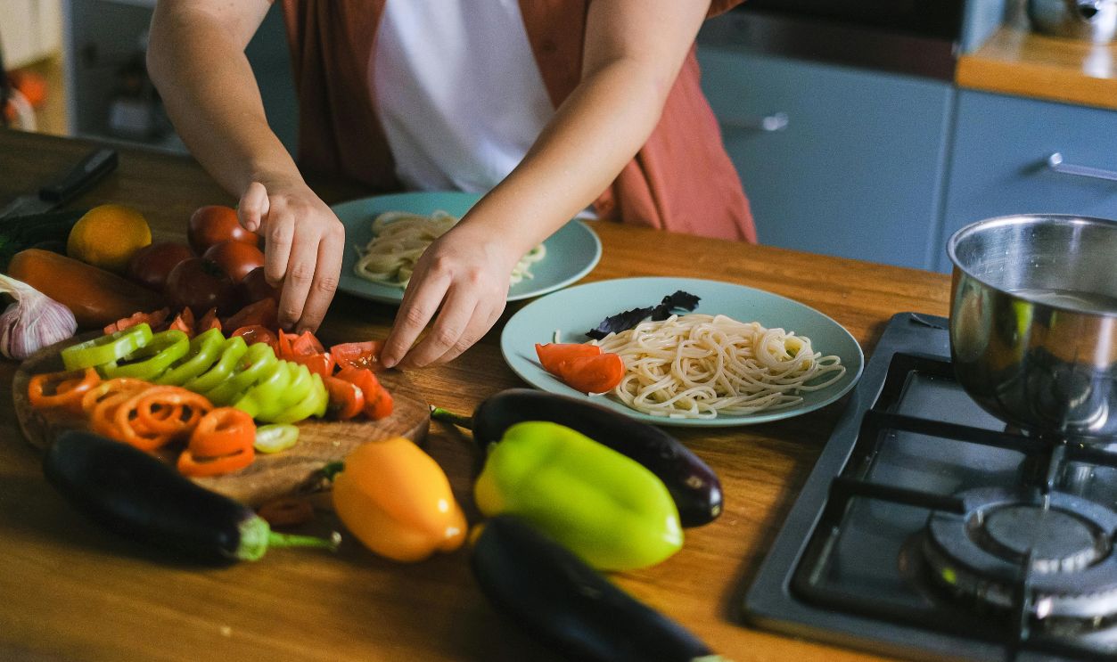 Woman arranging fresh vegetables and pasta on plates in a kitchen setting