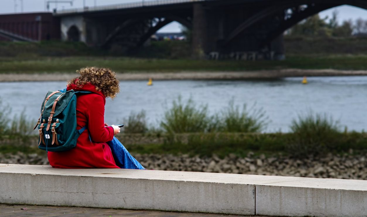 A woman sitting on a ledge looking at her cell phone