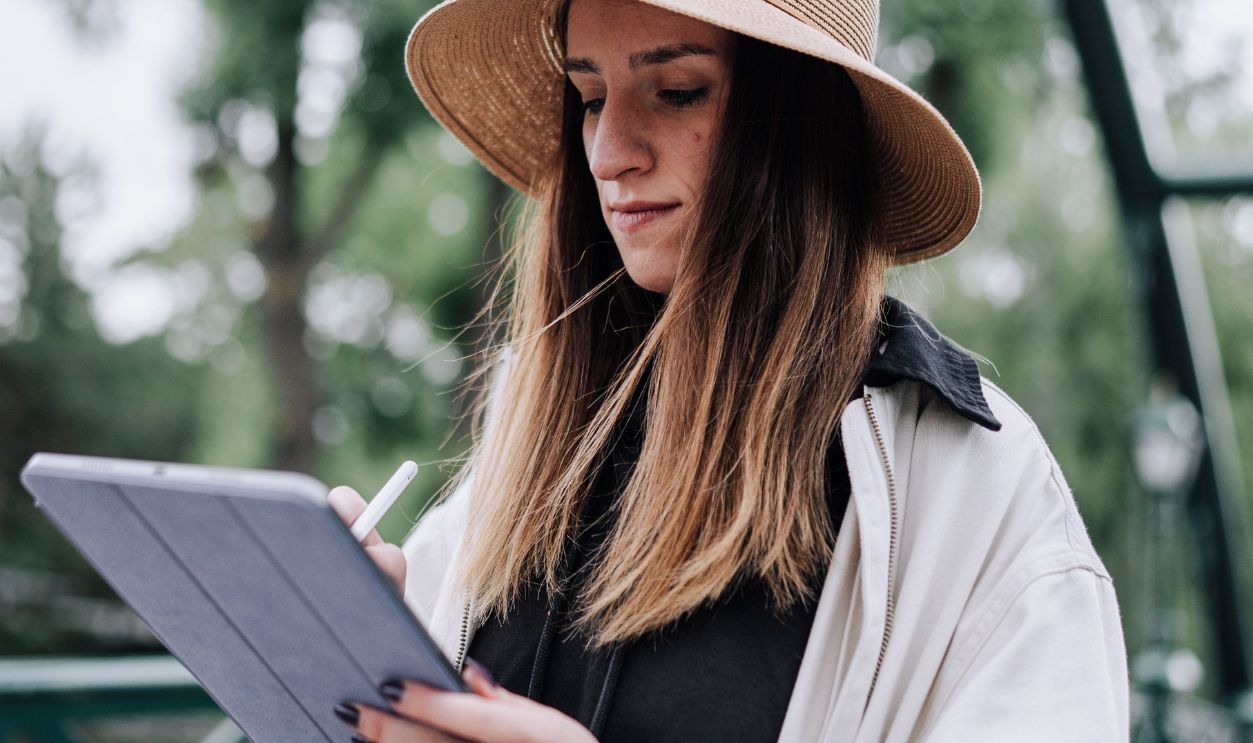 A woman in a hat uses a tablet outdoors, portraying modern lifestyle