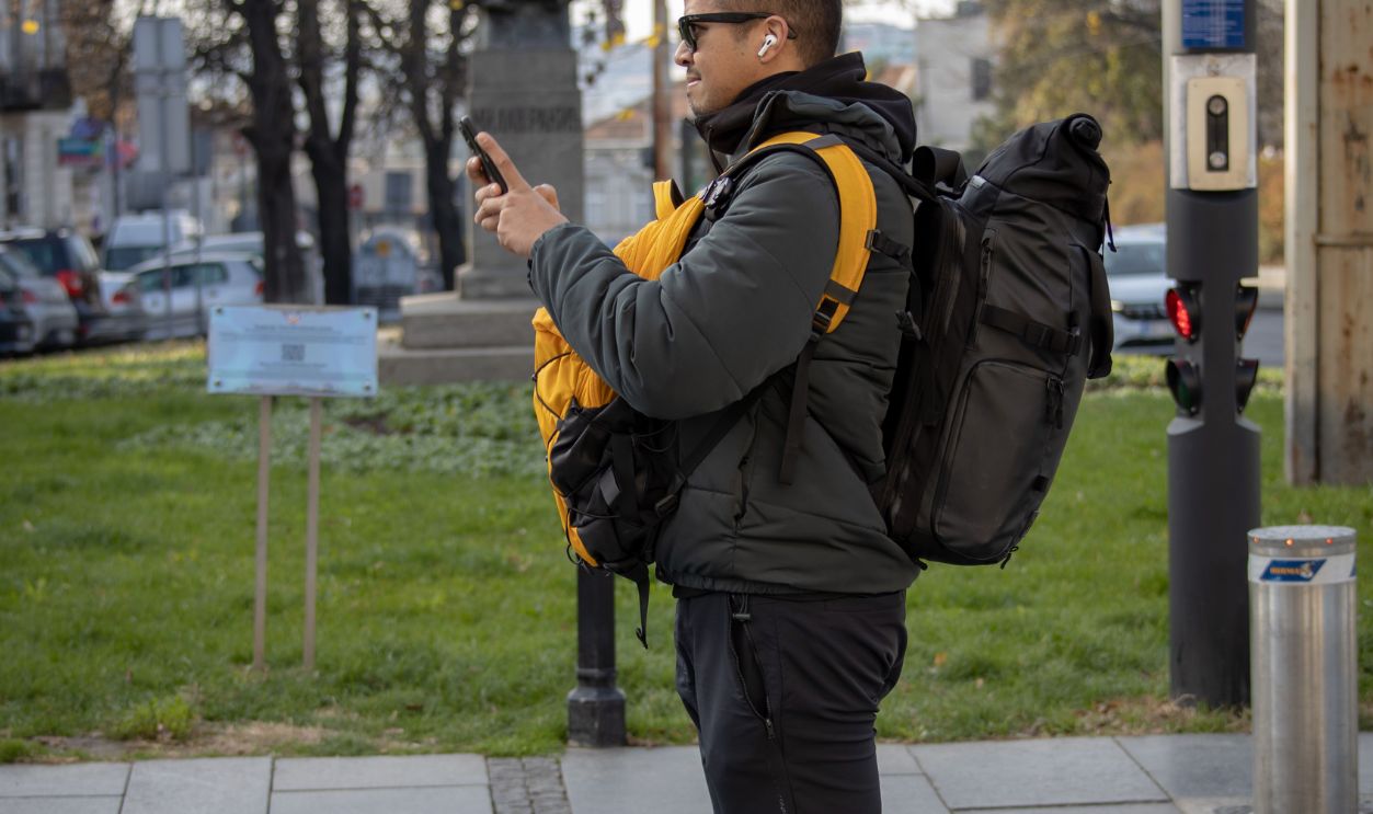 Man with a backpack texting outdoors in a city park during autumn