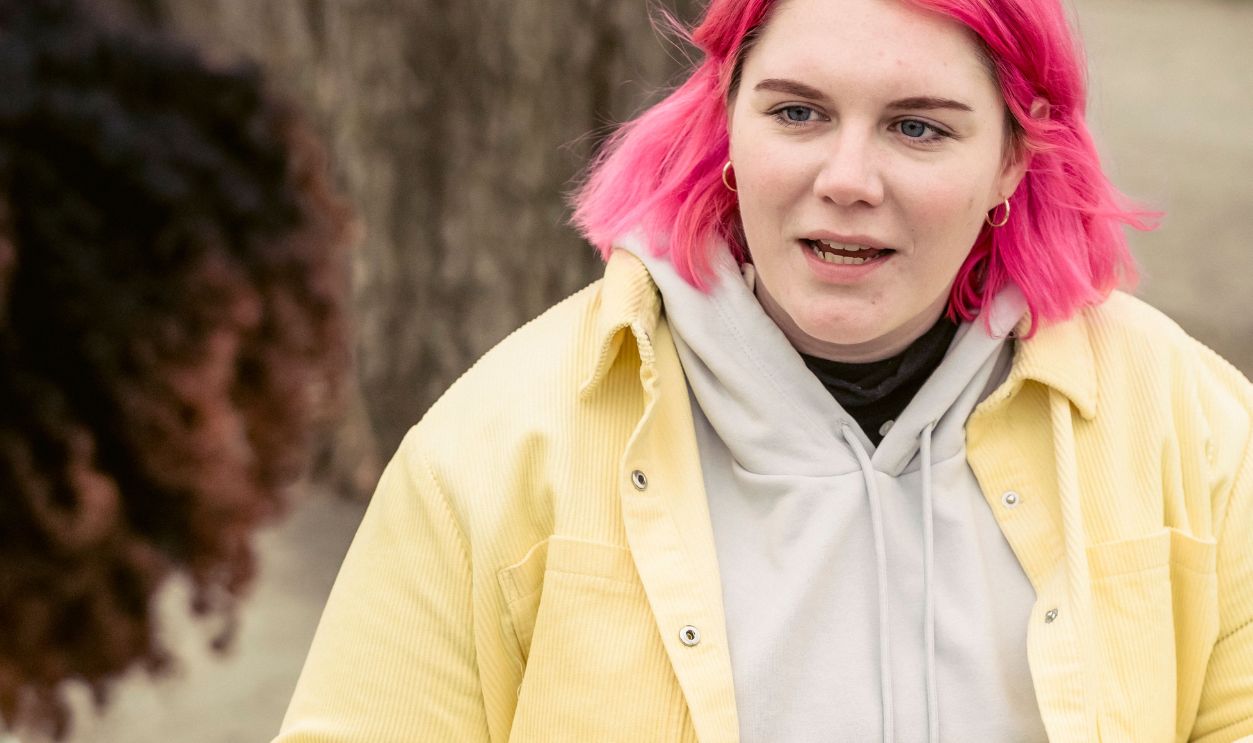 Two young women interact over drinks at an outdoor park table