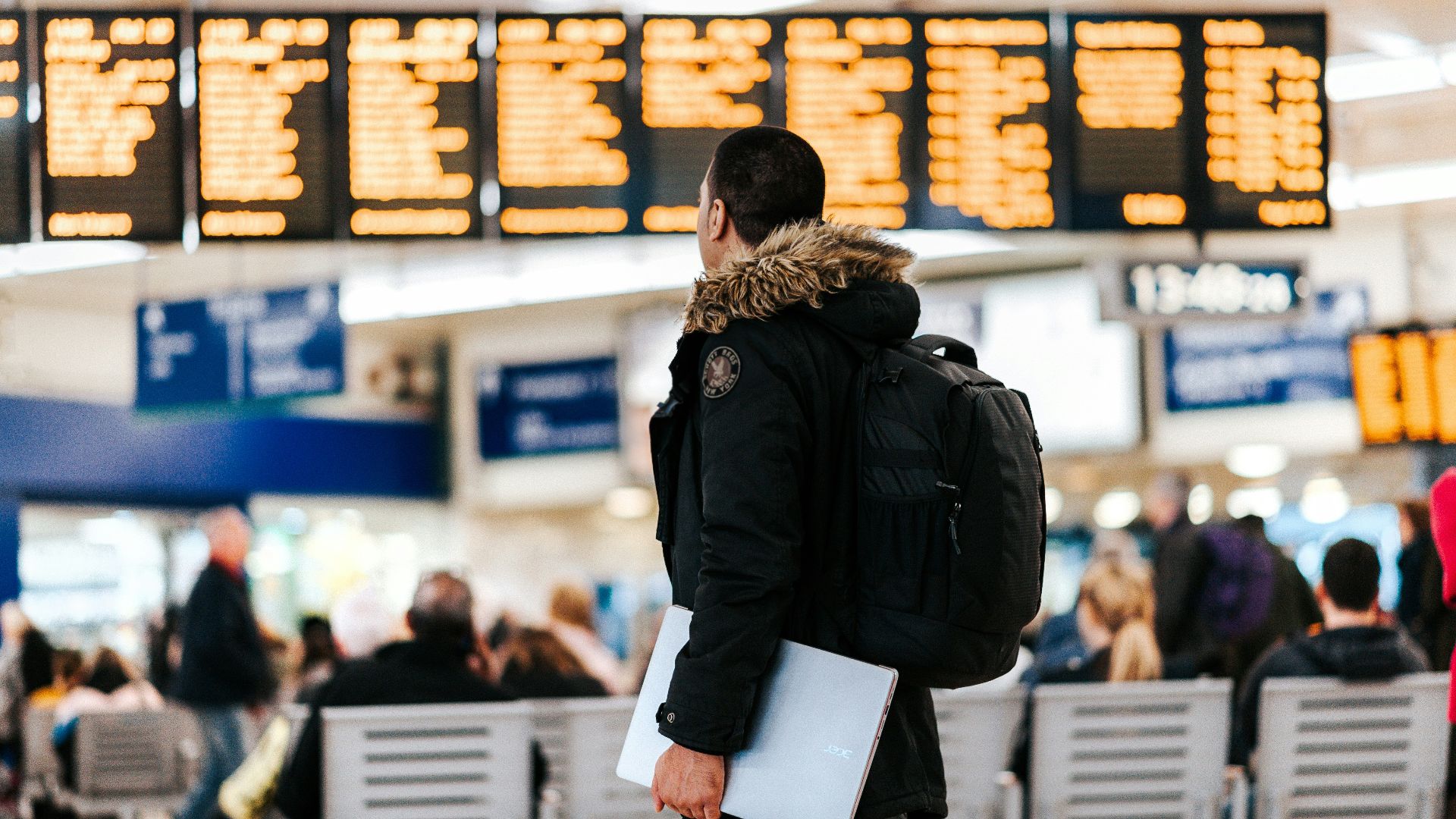 man standing inside airport looking at LED flight schedule bulletin board