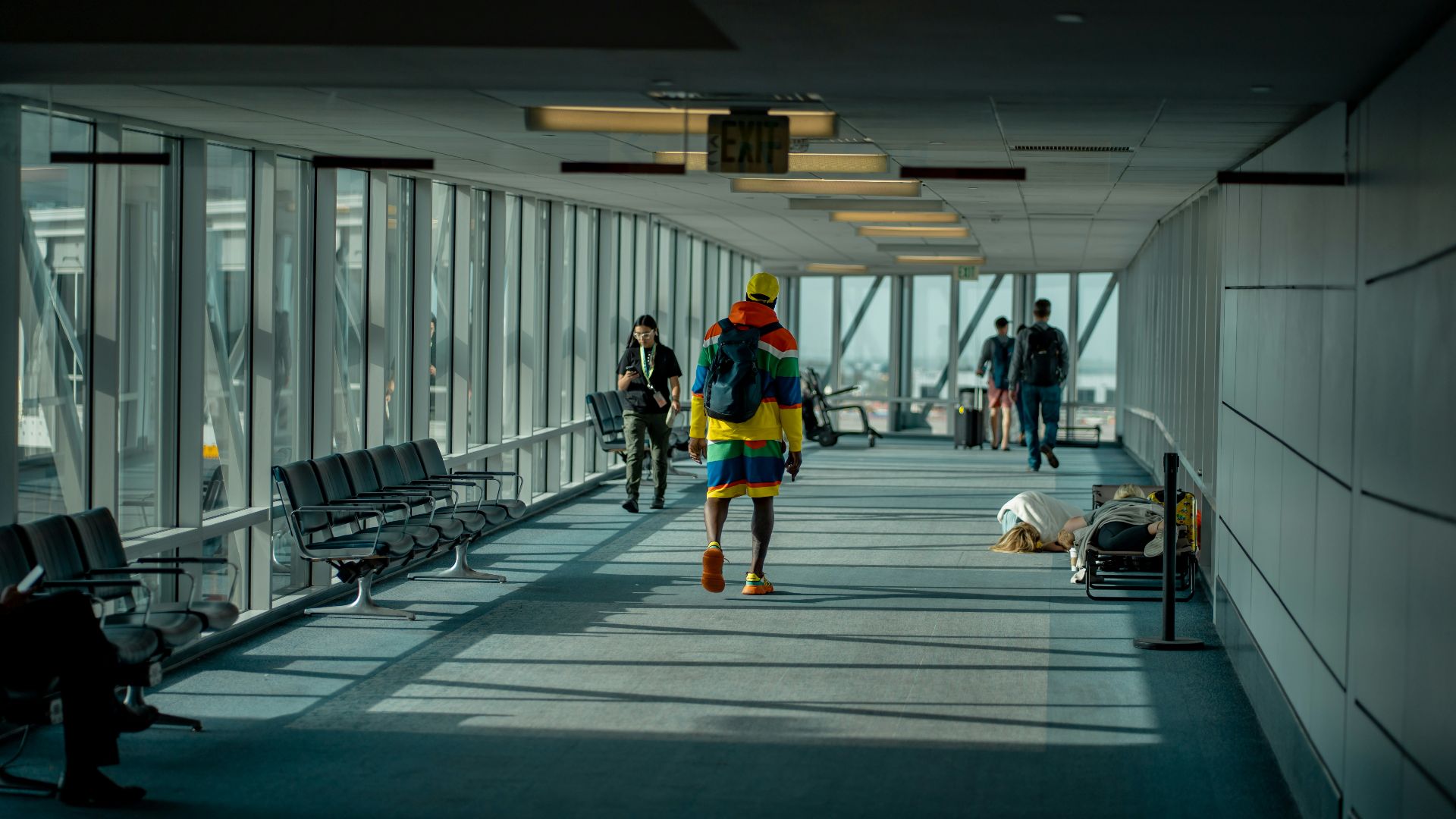 a man walking down a long hallway with lots of windows