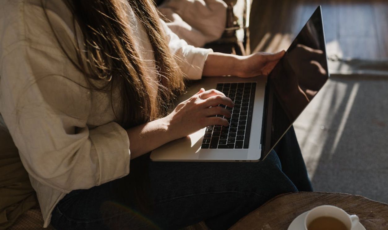 Close-up of a woman using a laptop in a warm, cozy indoor setting with sunlight