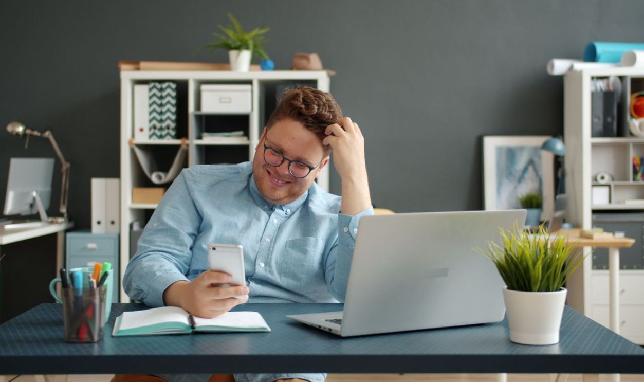 Smiling man in office using smartphone, engaged and relaxed