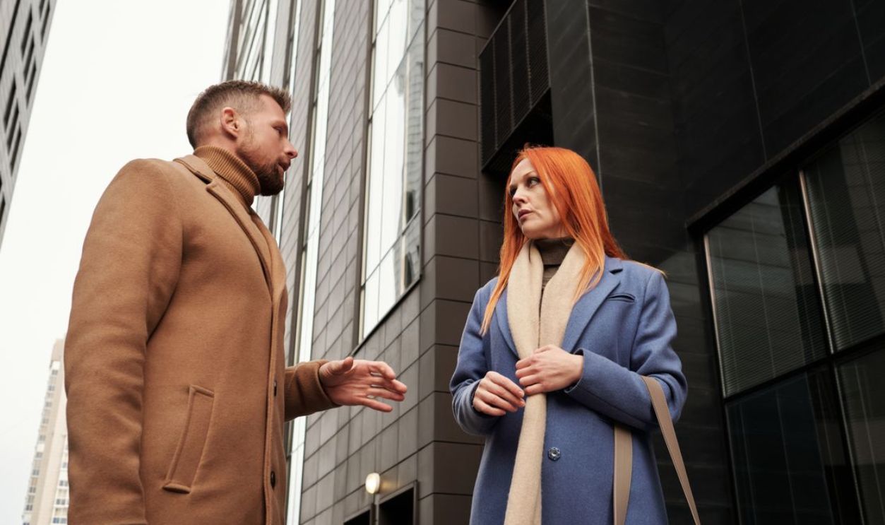 Two adults engage in a conversation outdoors between modern city buildings
