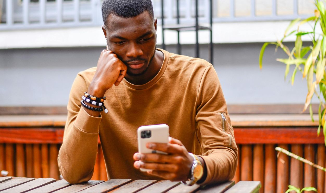 African American man sitting outside, using a smartphone, in thoughtful pose