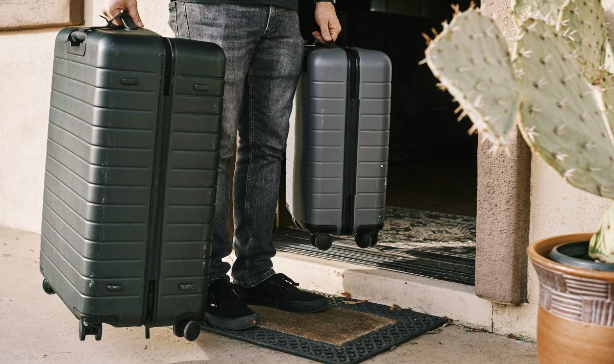 man in black denim jeans and black leather shoes standing beside black luggage bag