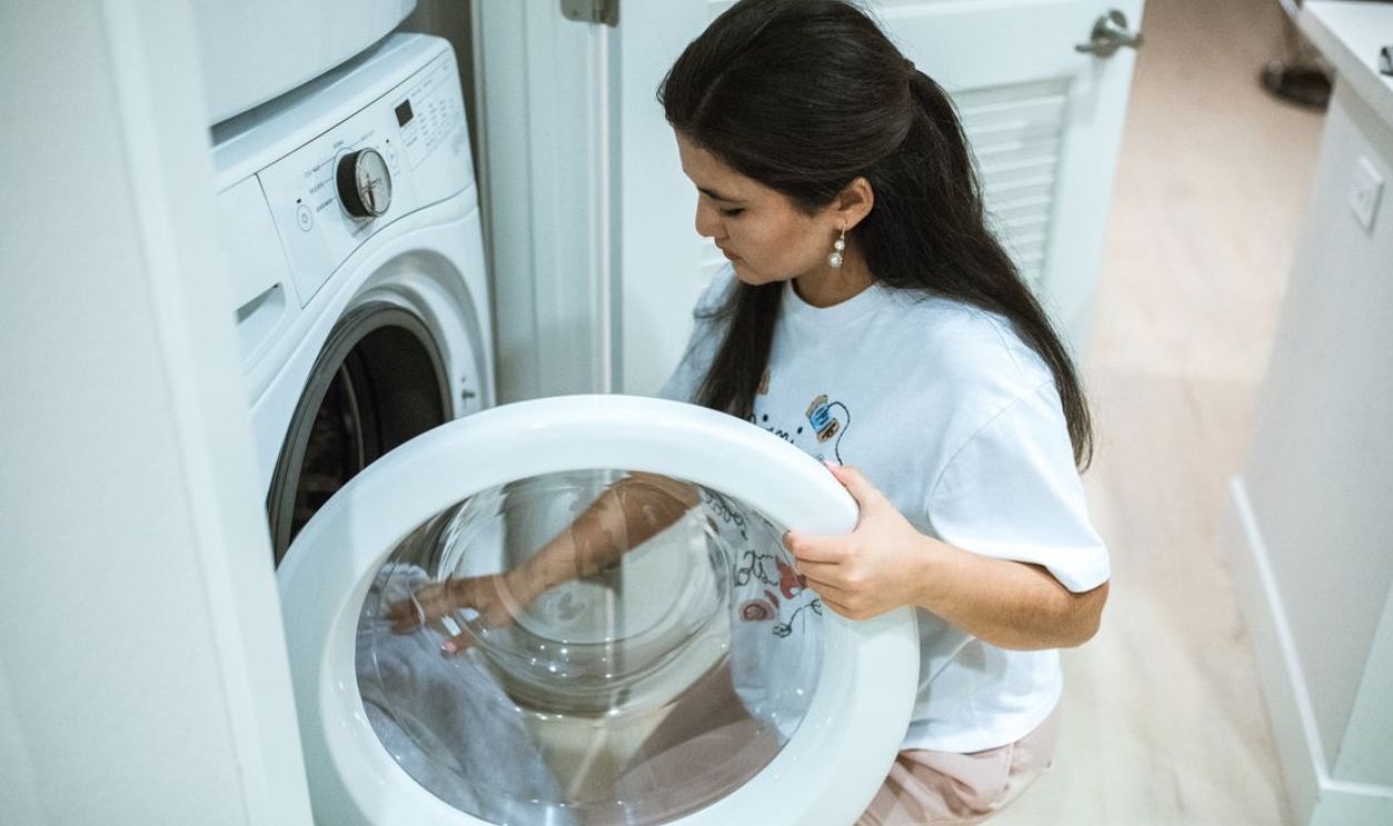 A woman kneeling to load clothes into a front-loading washing machine in a modern home laundry room