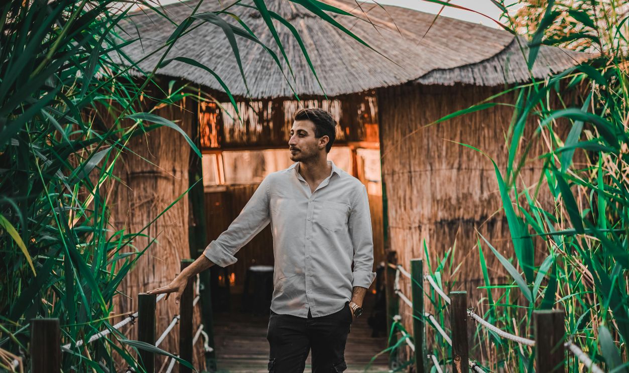 A man casually posing on a lush wooden bridge surrounded by greenery, evoking a sense of tranquility