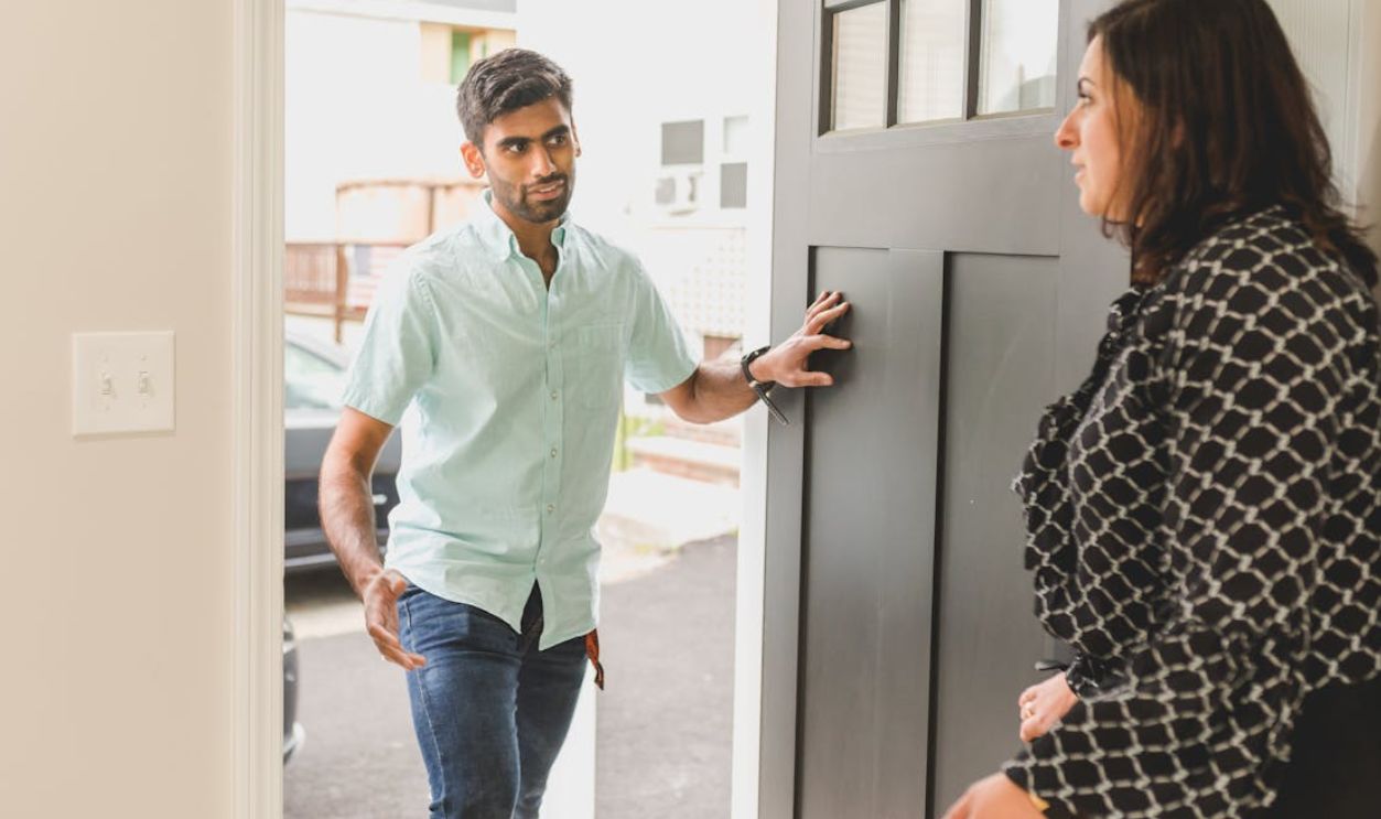 A man enters a home, conversing with a woman standing nearby in a casual setting