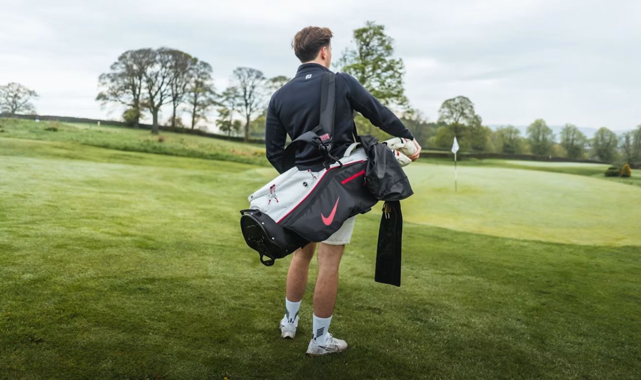 a man holding a golf bag on top of a lush green field