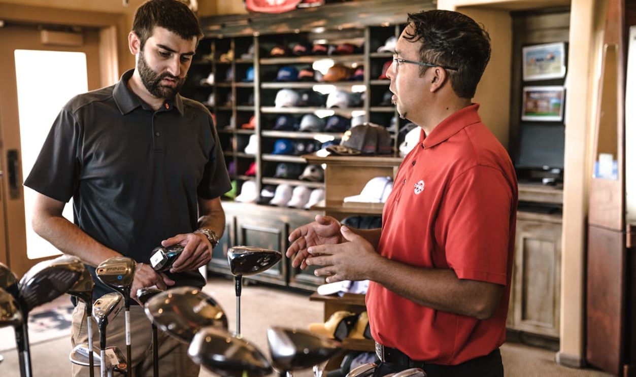 Customer receiving expert advice from salesman on golf equipment in a store.