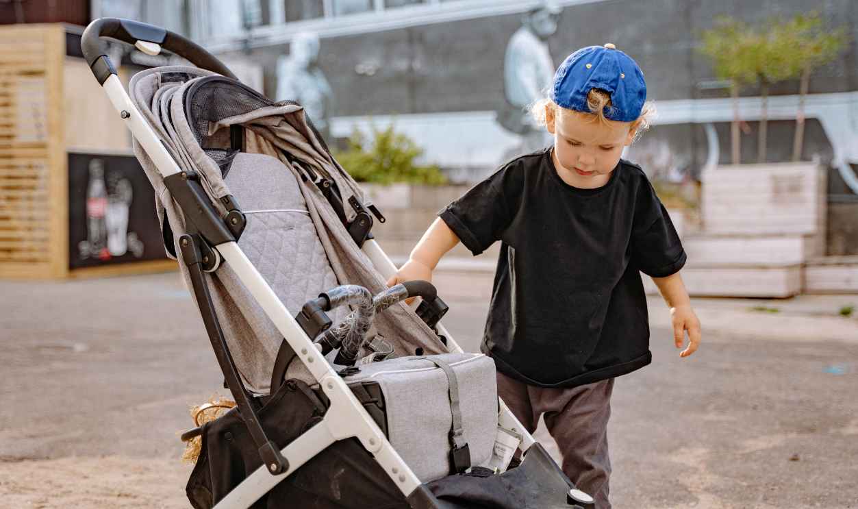 A young child in casual wear examines a stroller