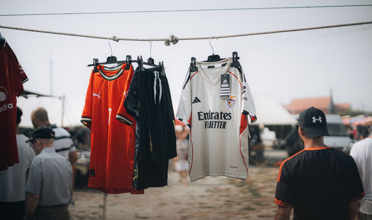 Colorful sports jerseys hanging at an outdoor market with people
