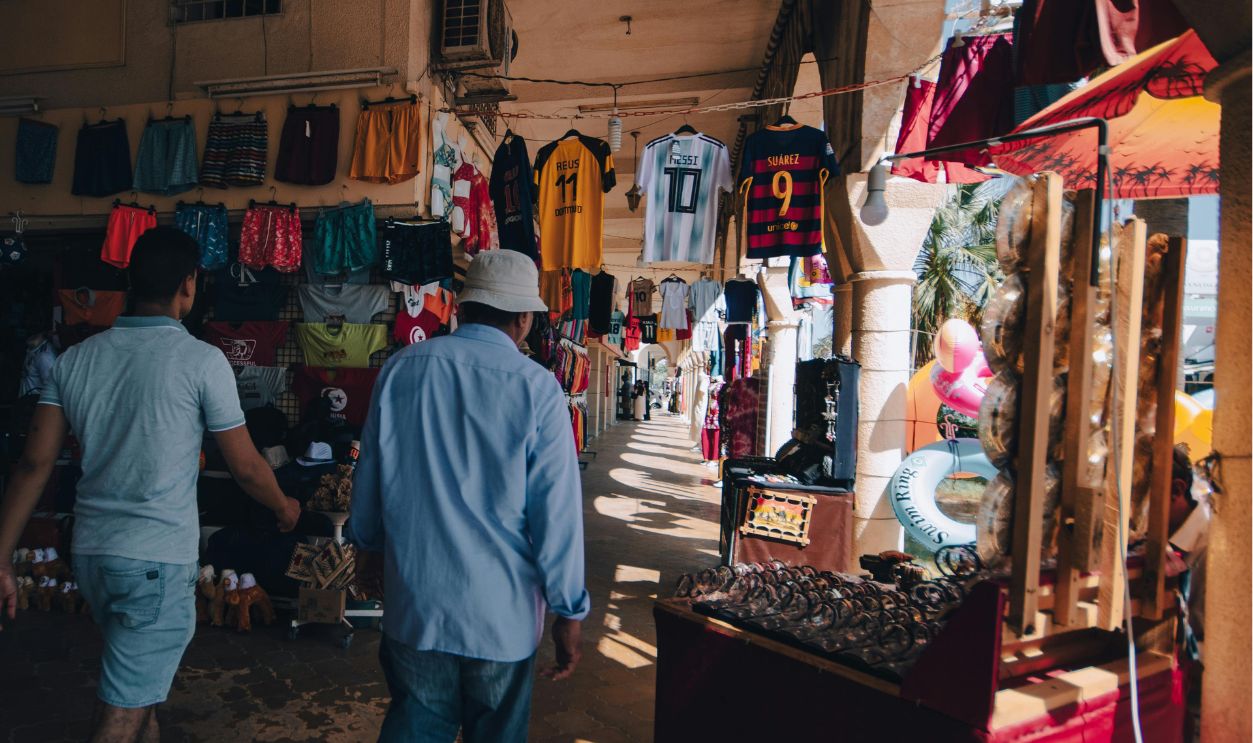 Two men walk through a vibrant clothing market