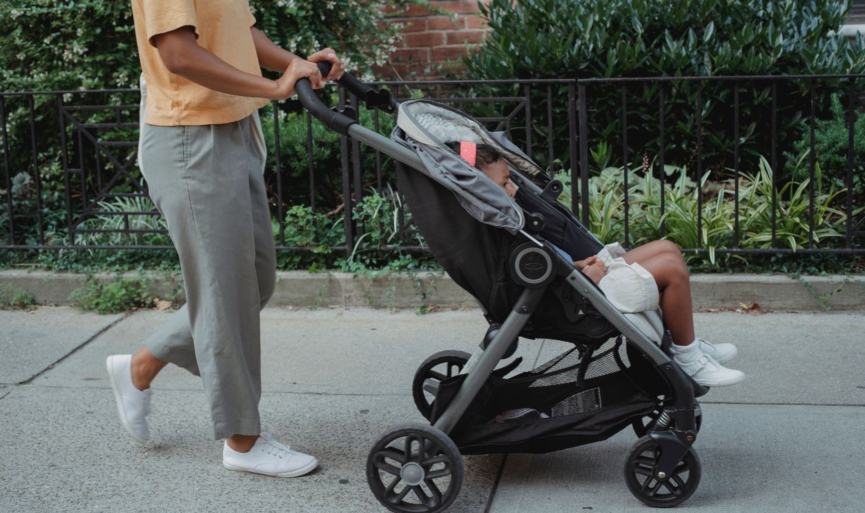 A mother walks with her toddler in a stroller on a city sidewalk