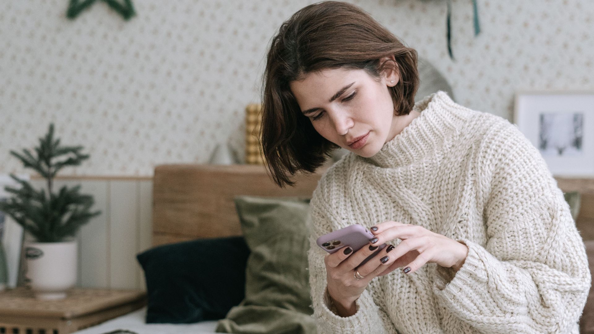 A woman in a cozy sweater using her phone in a beautifully decorated bedroom.