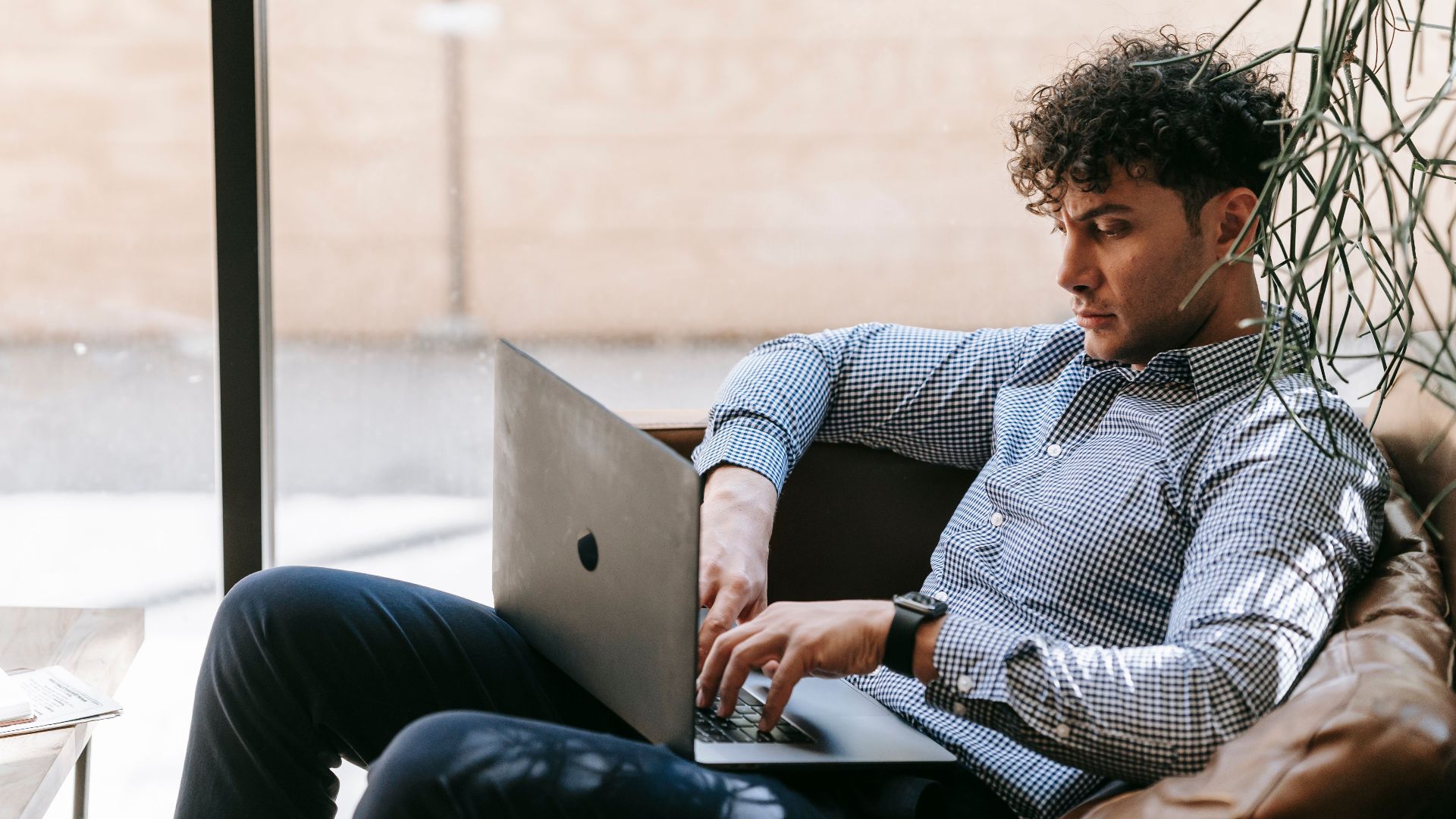 A man in smart casual attire using a laptop on a couch indoors.
