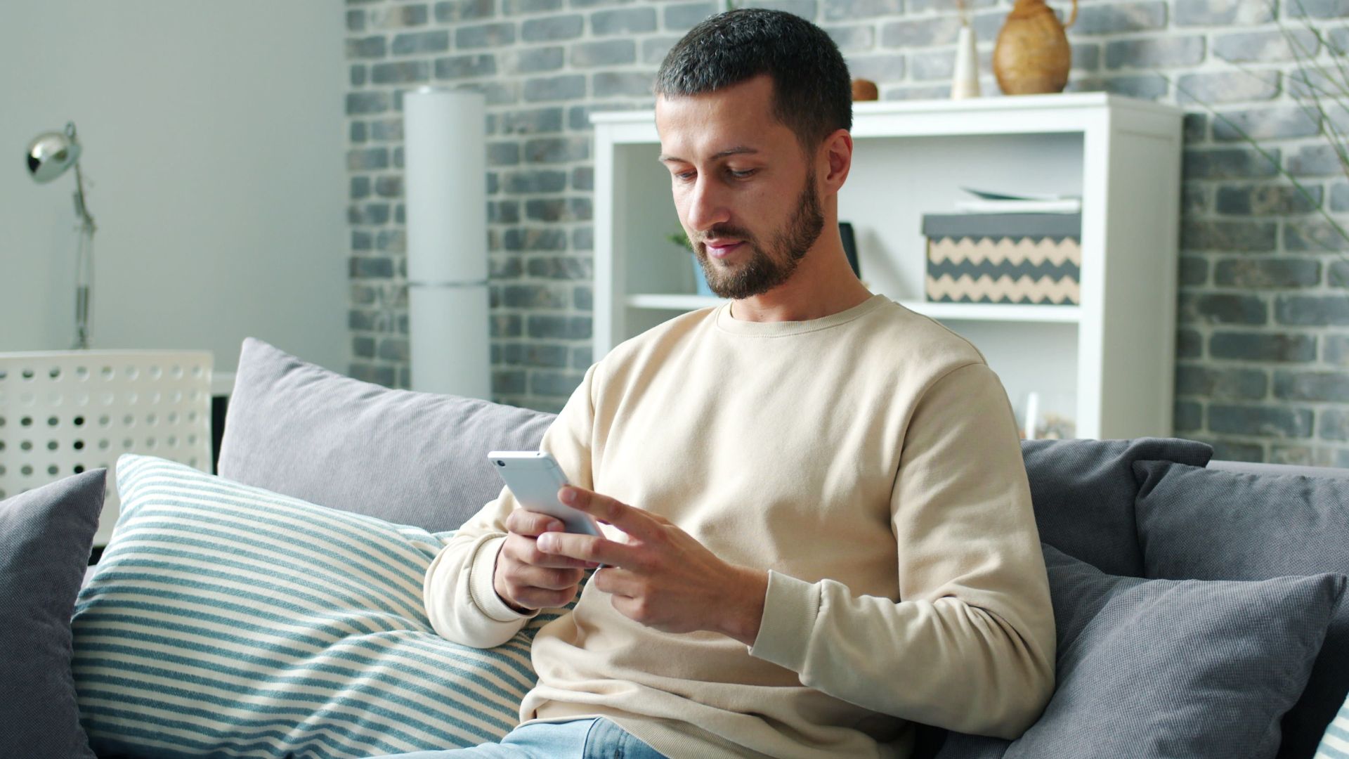 Man sitting on a couch using a smartphone in a cozy living room setting.