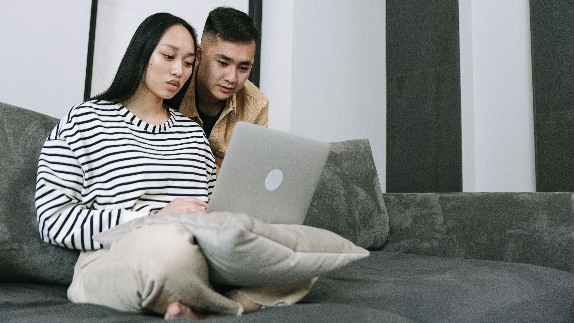 Young couple seated on sofa using laptop together in modern living room.