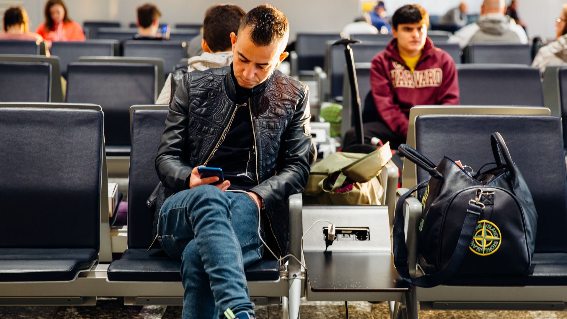 People sitting in an airport lounge, focused on smartphones and waiting for flights.