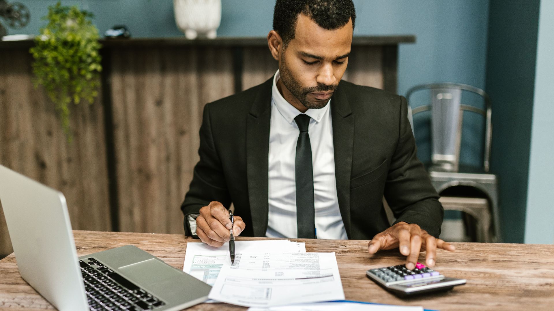 A focused businessman works with a calculator and documents in a modern office.