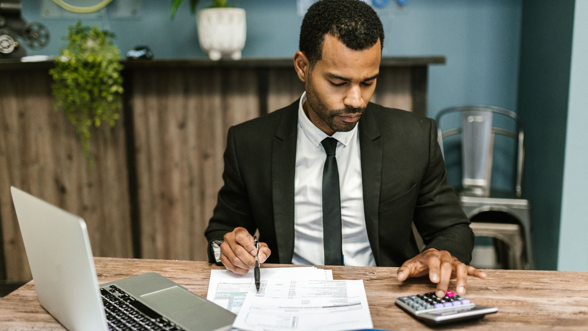 A focused businessman works with a calculator and documents in a modern office.