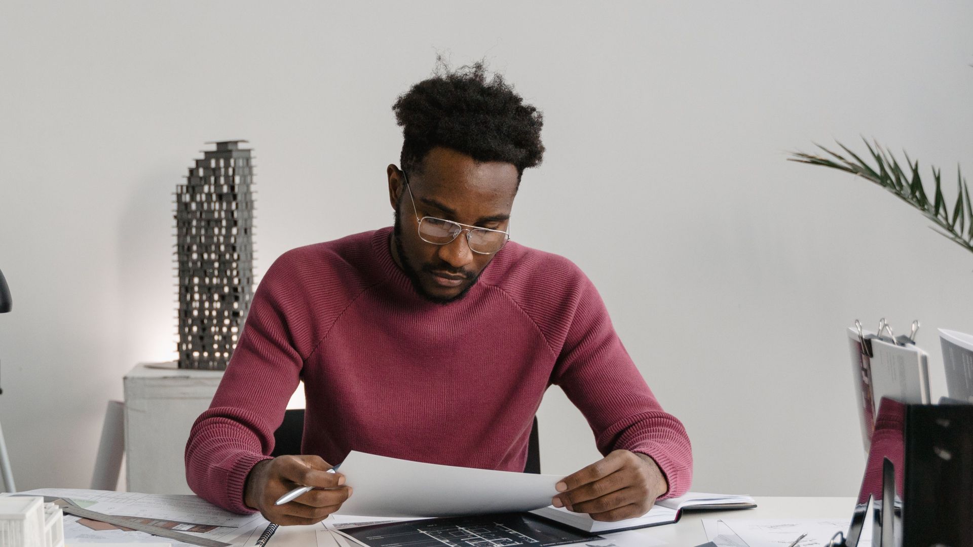 Architect working on designs at a desk cluttered with planning materials and tools.