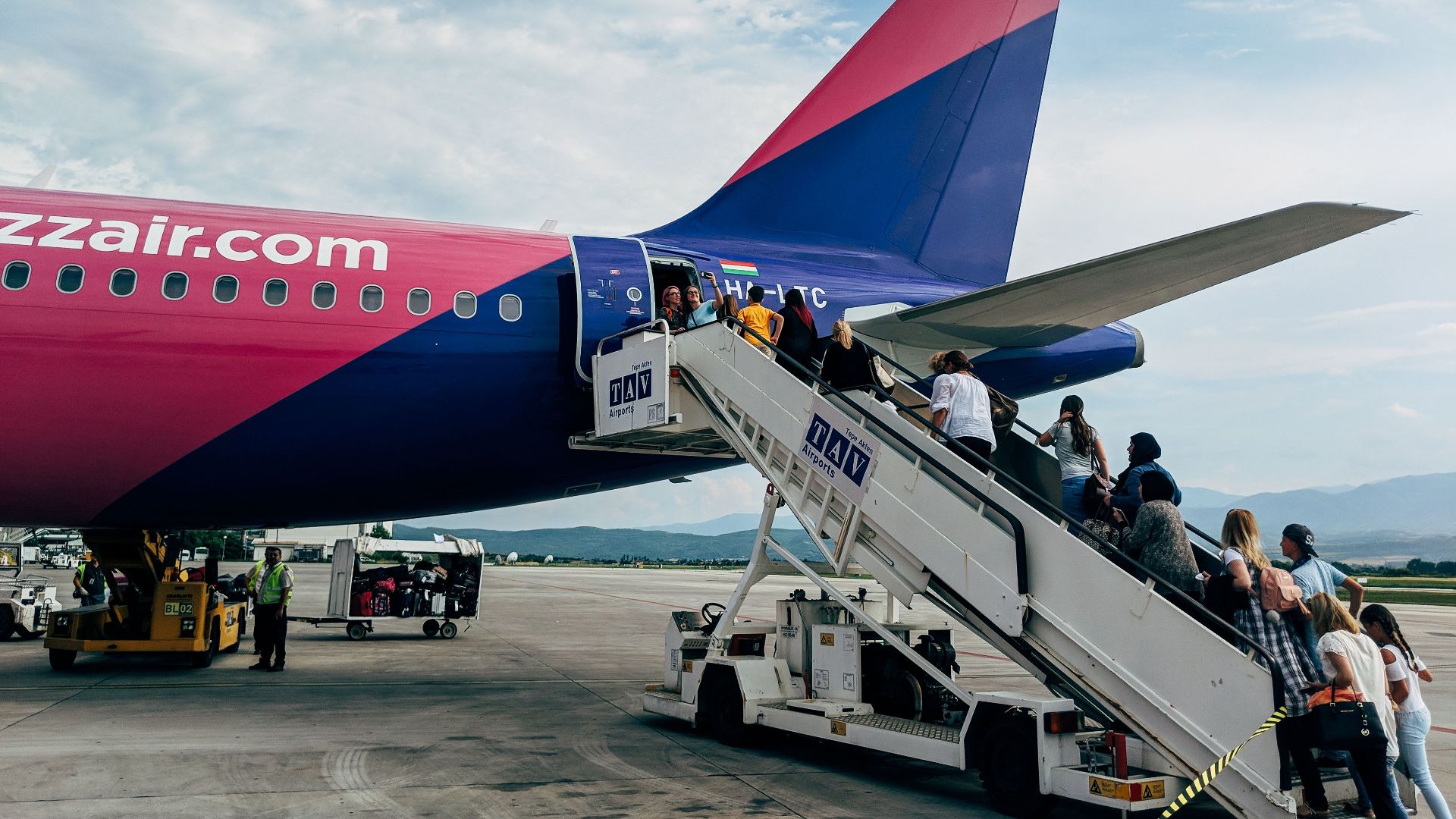Travelers boarding a WizzAir Airbus A320 jet on a clear day at the airport.