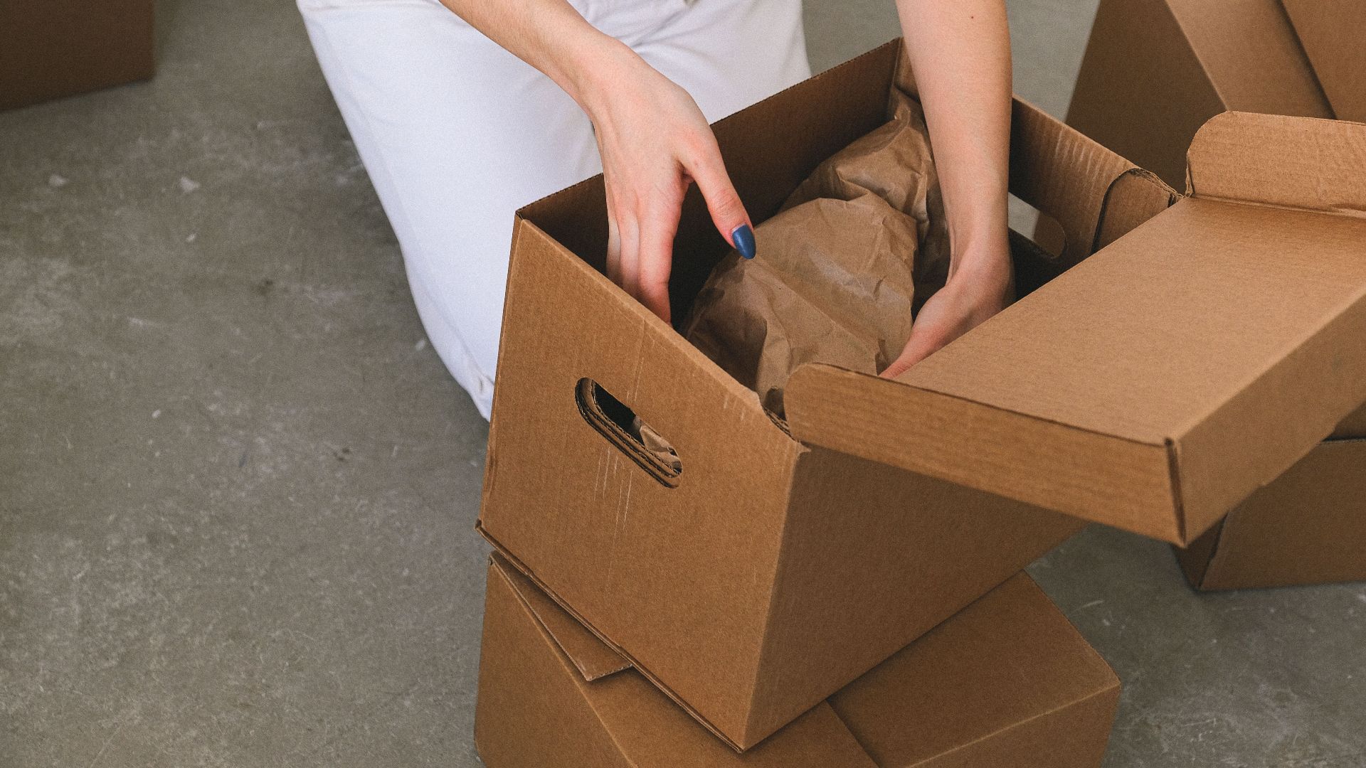 From above of crop anonymous relocating female packing wrapped items into carton box while preparing for moving to new apartment