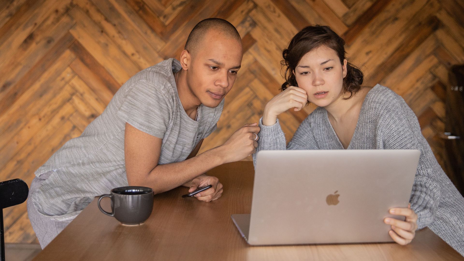 Concentrated diverse friends in casual clothes surfing laptop while sitting together at wooden table