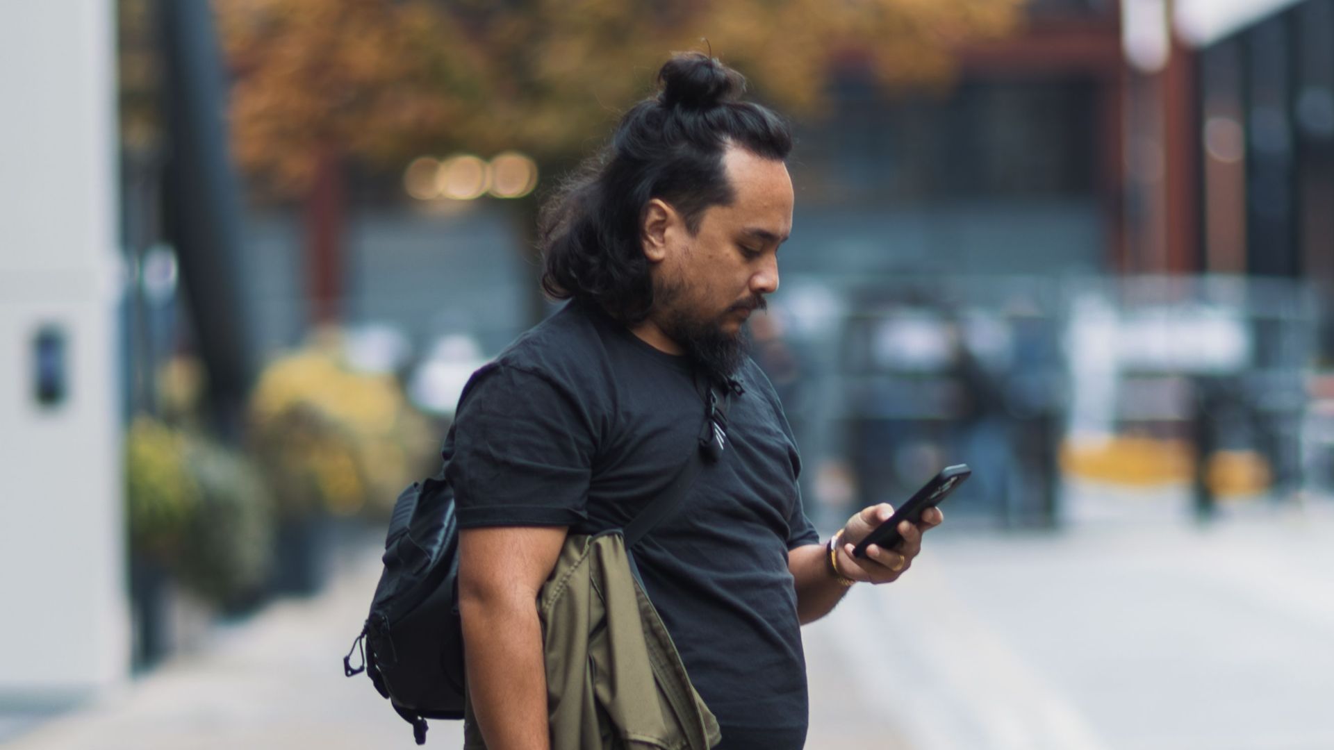Photographer checks phone while holding camera on city street.